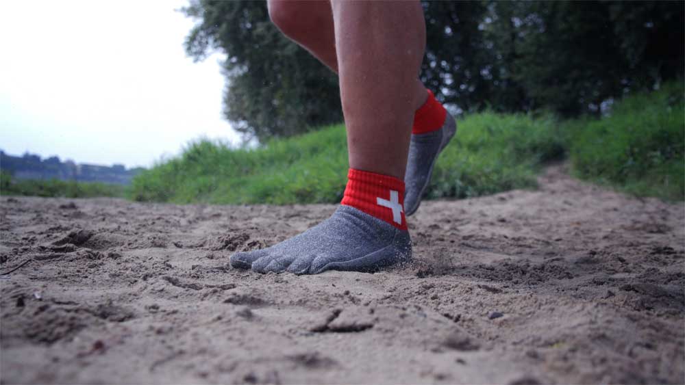 Man sieht einen Sandboden. Jemand hat die Free Your Feet Socken an und läuft damit über den Sand.