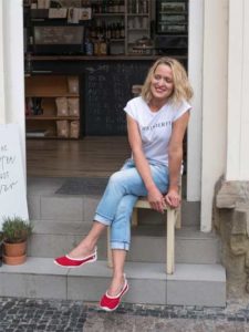 Eine Fraue sitzt am Eingang eines Geschäfts, an den Füßen die Ballerinas von Joe Nimble in rot