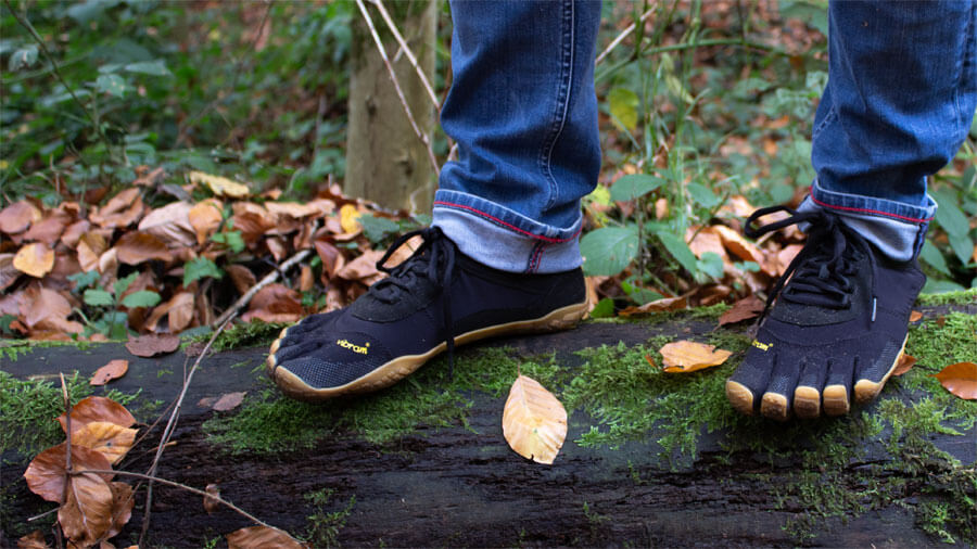 Der Autor steht steht mit dem Vibram V-Trek in schwarz auf einem Baumstamm.